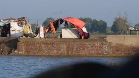 Static-shot-of-makeshift-camps-of-dispalced-families-in-the-background-with-flood-water-flowing-in-the-front-in-Sindh,-Pakistan-at-daytime