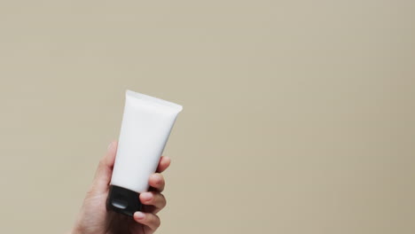 hand of woman holding tube with cream on beige background with copy space, slow motion