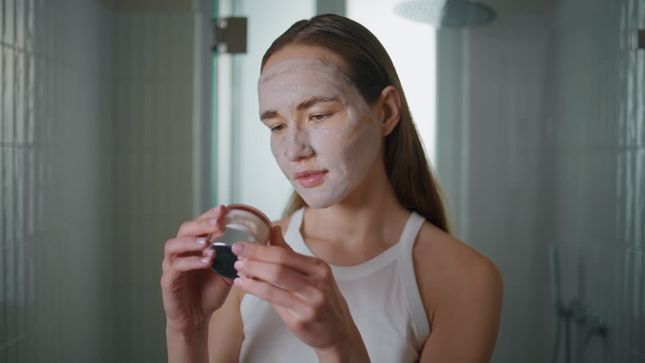 Home girl applying mask on face in morning. Closeup woman reading cream bottle