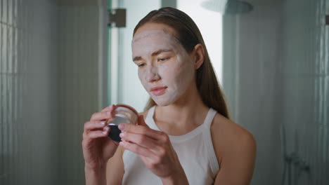 home girl applying mask on face in morning. closeup woman reading cream bottle
