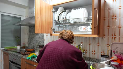 elderly woman in purple clothing cleaning and organizing dishes in a home kitchen