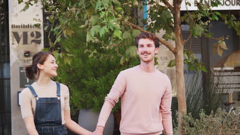 happy young hipster couple walking in city street holding hands, close up