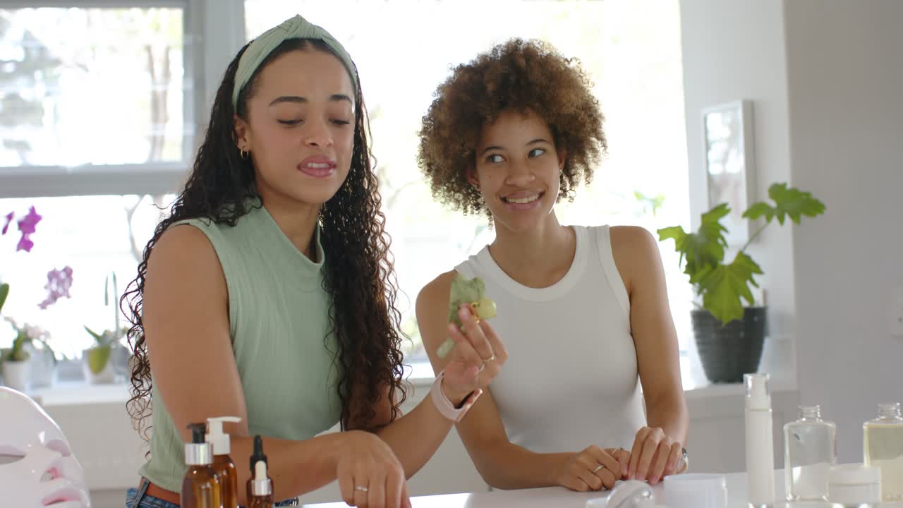 2 African American women left reaching amber vials showing green tool teaching skin tips at counter