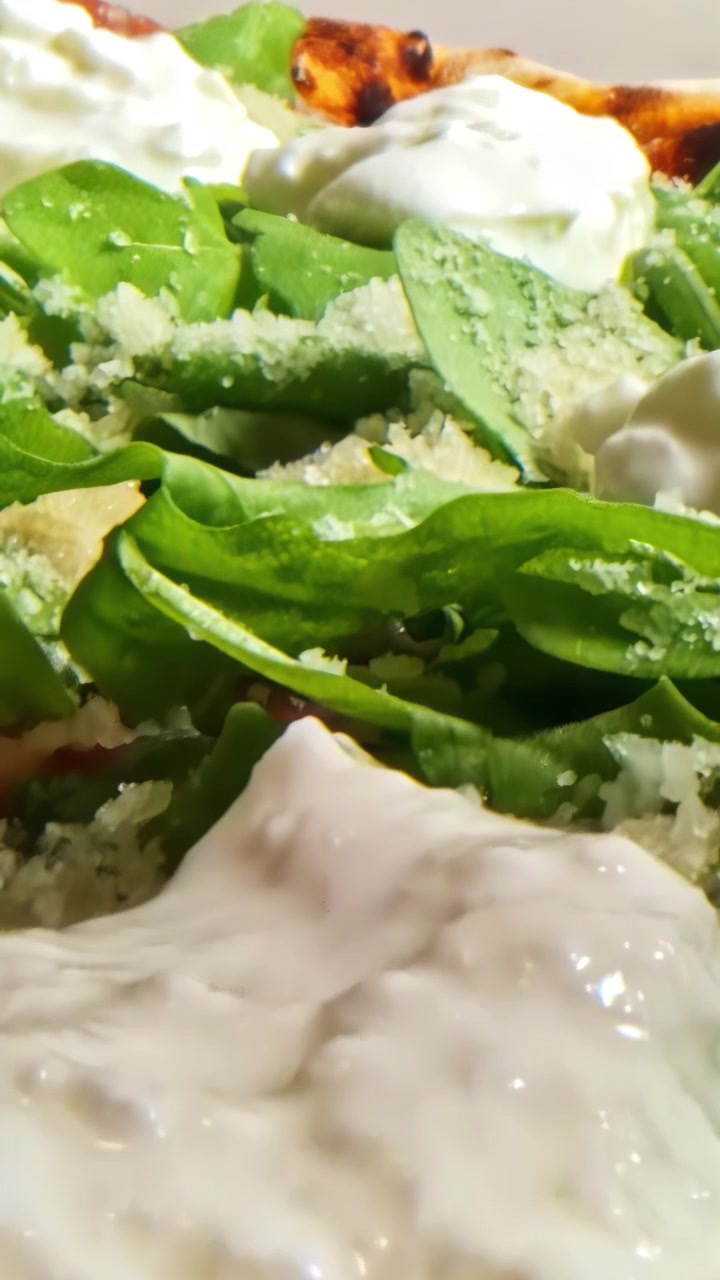 Scatto macro di una pizza artigianale fresca condita con cremosa burrata, rucola verde e parmigiano. Dettaglio culinario cinematografico per il marketing di ristoranti e gastronomia
