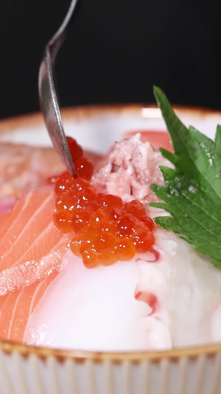 Cận cảnh đầu bếp thêm trứng cá hồi vào tô sushi chirashi đầy màu sắc.