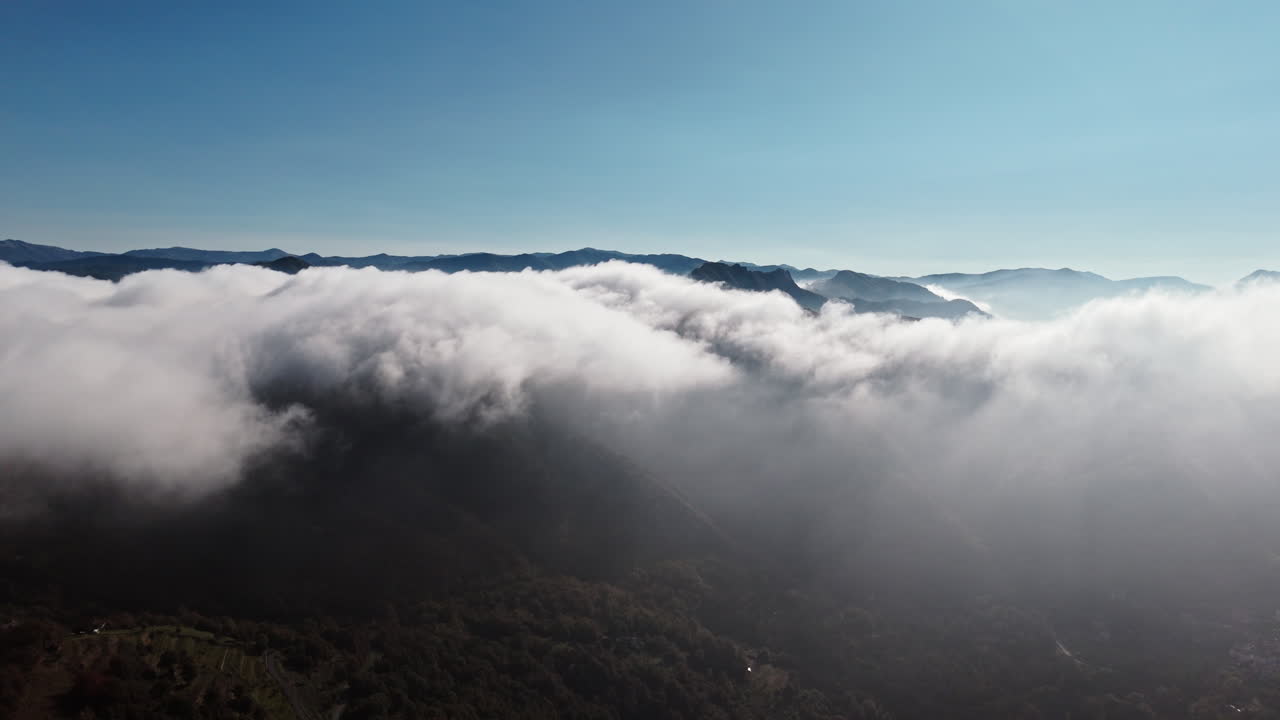 Mountain tops covered in clouds during a tranquil sunny day, aerial view
