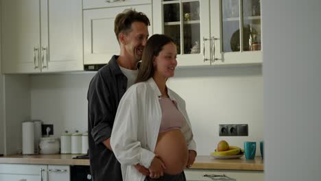 Happy-man-behind-his-pregnant-wife-holds-her-by-the-waist-and-dances-in-the-morning