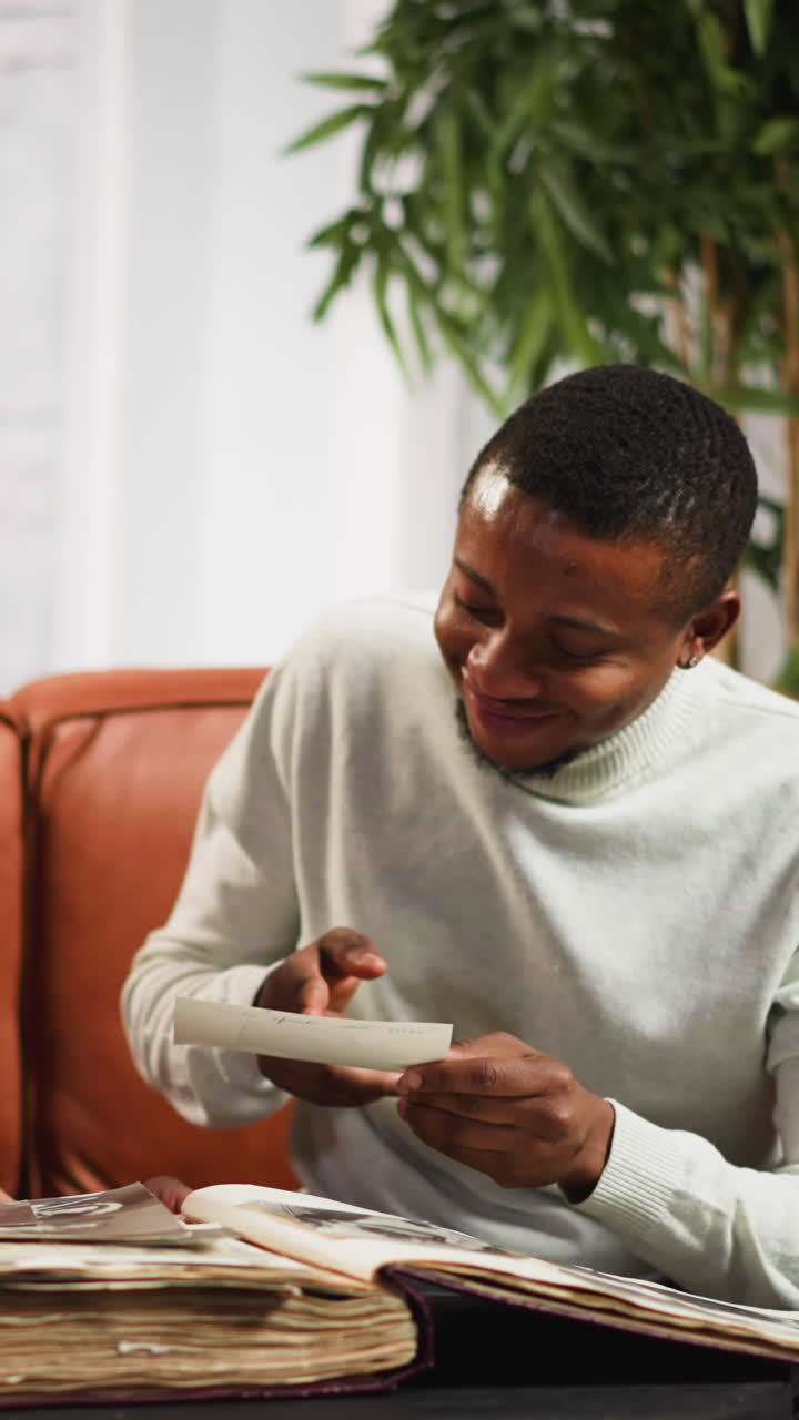 Surprised black man likens young blonde woman friend with grandmother on vintage picture from photoalbum on couch in living room slow motion
