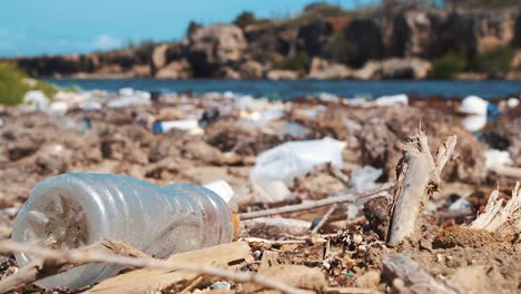 Rack-focus-on-plastic-water-bottle-littered-on-dirty-beach,-Closeup