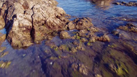 Drone-flying-over-the-sea-on-a-rocky-coastline,-moving-higher-to-reveal-the-Mediterranean-sea