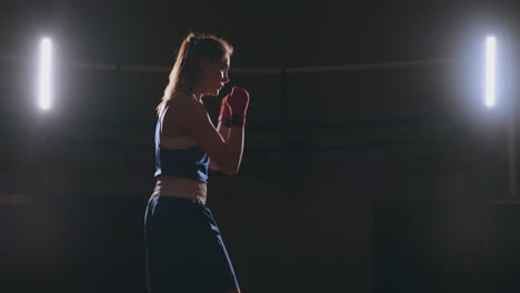 A-beautiful-woman-boxer-trains-in-a-dark-gym-and-works-out-punches-in-slow-motion.-Camera-movement-side-View.-Steadicam-shot