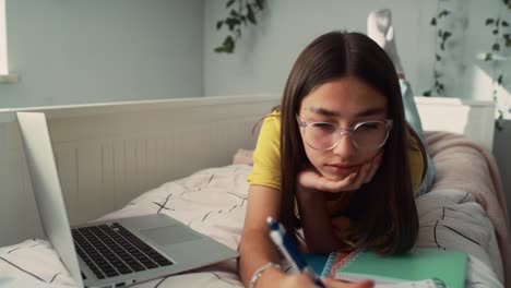 Adolescente-Caucásica-Acostada-En-La-Cama-En-El-Frente-Y-Haciendo-La-Tarea