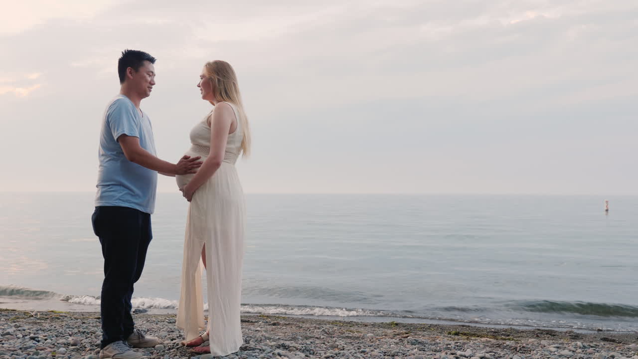 젊은 다민족 부부가 해변에 서 있다 임신한 여자와 아시아 남자 다민족 공동