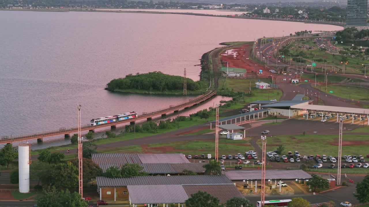 Aerial view of coastline and small peninsula with tramline and water surroundings at sunset, Posadas, Misiones, Argentina.