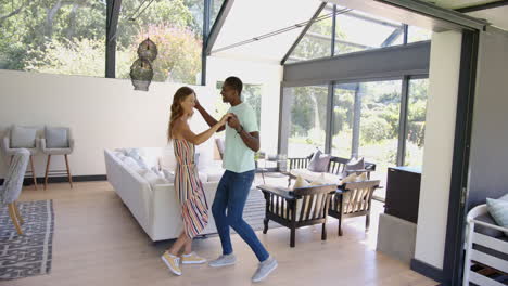 dancing together, diverse couple enjoying time in modern living room with large windows