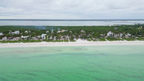 tropical beach with turquoise water, white sand, lush greenery, and coastal homes