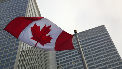 Disparo-En-ángulo-Bajo,-Vista-En-ángulo-Bajo-De-La-Bandera-De-Canadá-Ondeando-En-El-Viento-Y-Rascacielos-Como-Fondo