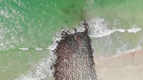 aerial view of waves breaks on rocks, bird's eye view of ocean waves crashing against the bare stones, deep blue sea with crashing waves and foam on rocks