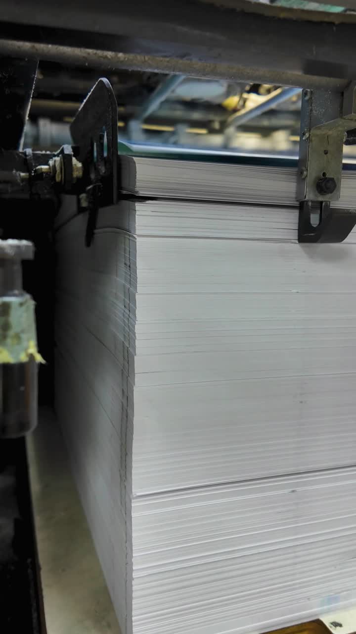 Large stack of printed paper sheets comes out of printing press industrial machinery, close up