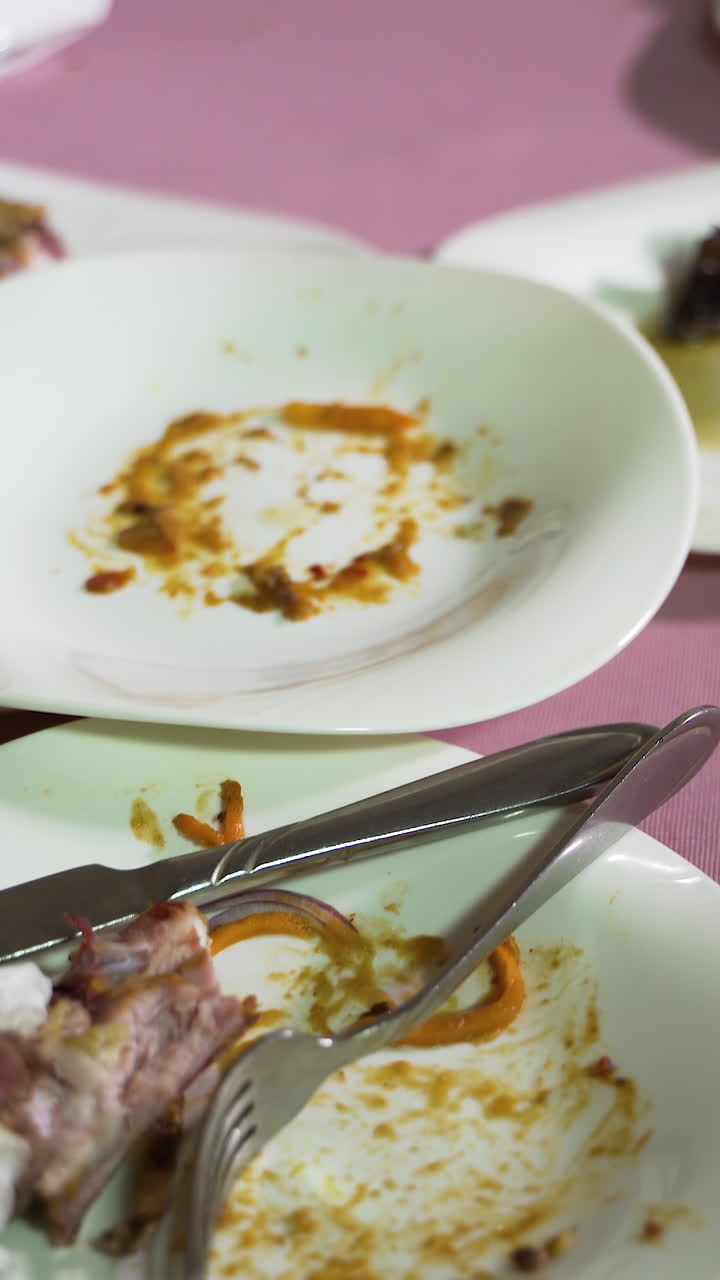 white porcelain plates with remnants of dishes are on a pink tablecloth on the table in the cafe. Camera motion to right Vertical video