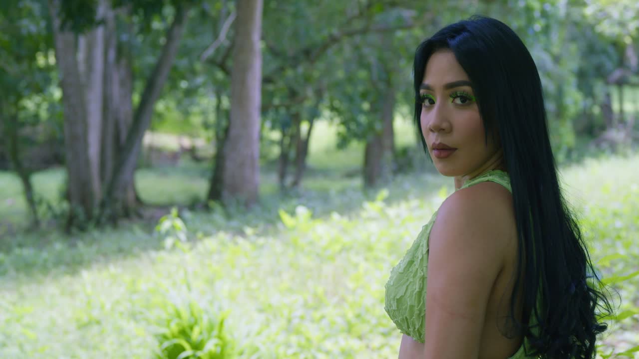 한 어린 소녀가 열대 공원에 서 있는 동안 그녀의 머리를 가지고 논다