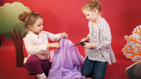 little girls cut a piece of cloth with scissors. studio shooting of children