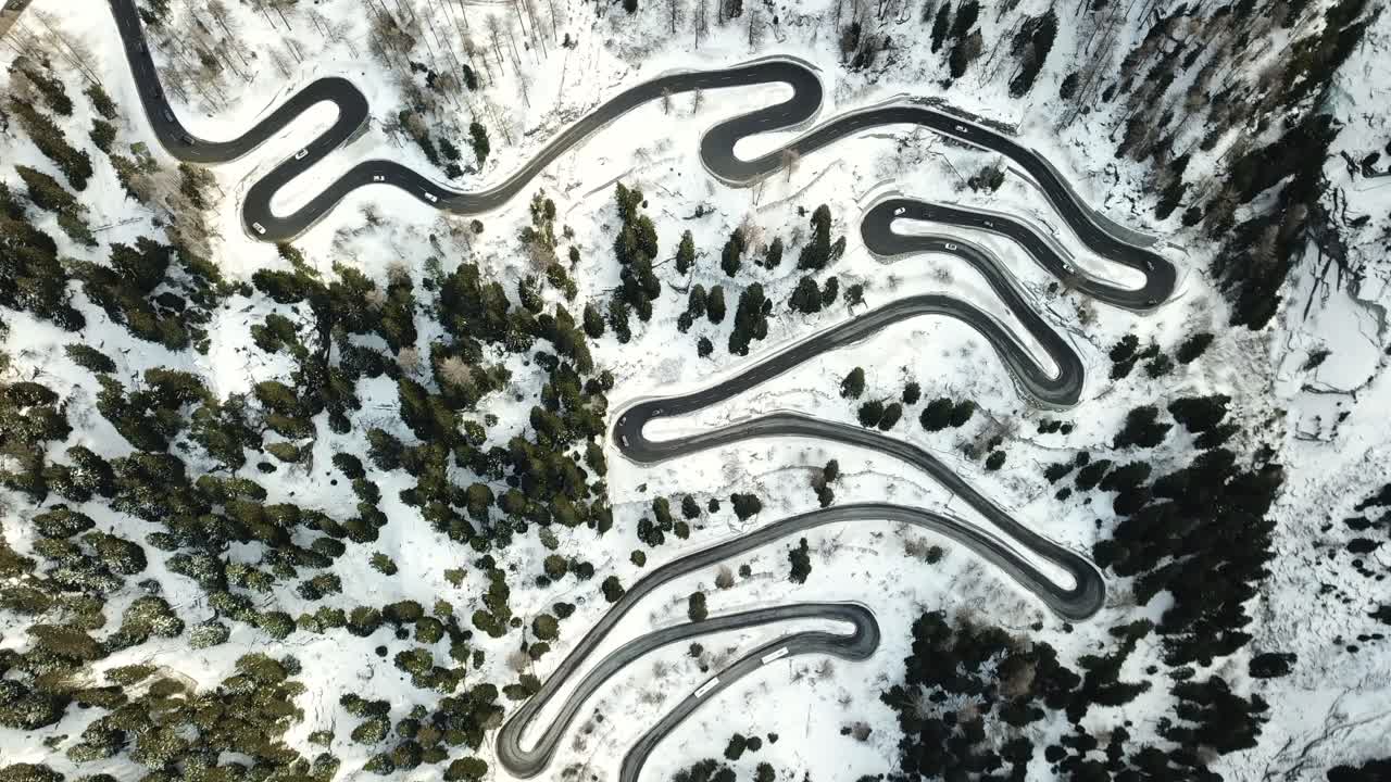 Aerial top-down descends on a winding road through Malojapass in Graubünden, Switzerland, showcasing the curves of the alpine road in a snowy landscape
