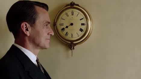 a man in a suit stands in profile next to an ornate wall clock