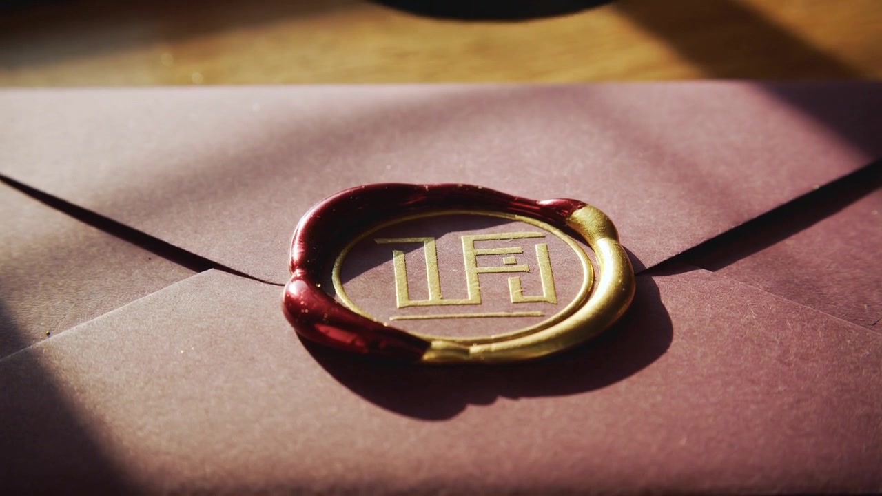 Abbassando un sigillo con manico scuro che preme cera rosso-oro su una busta bordeaux su un tavolo, sigillando con un sigillo dorato.