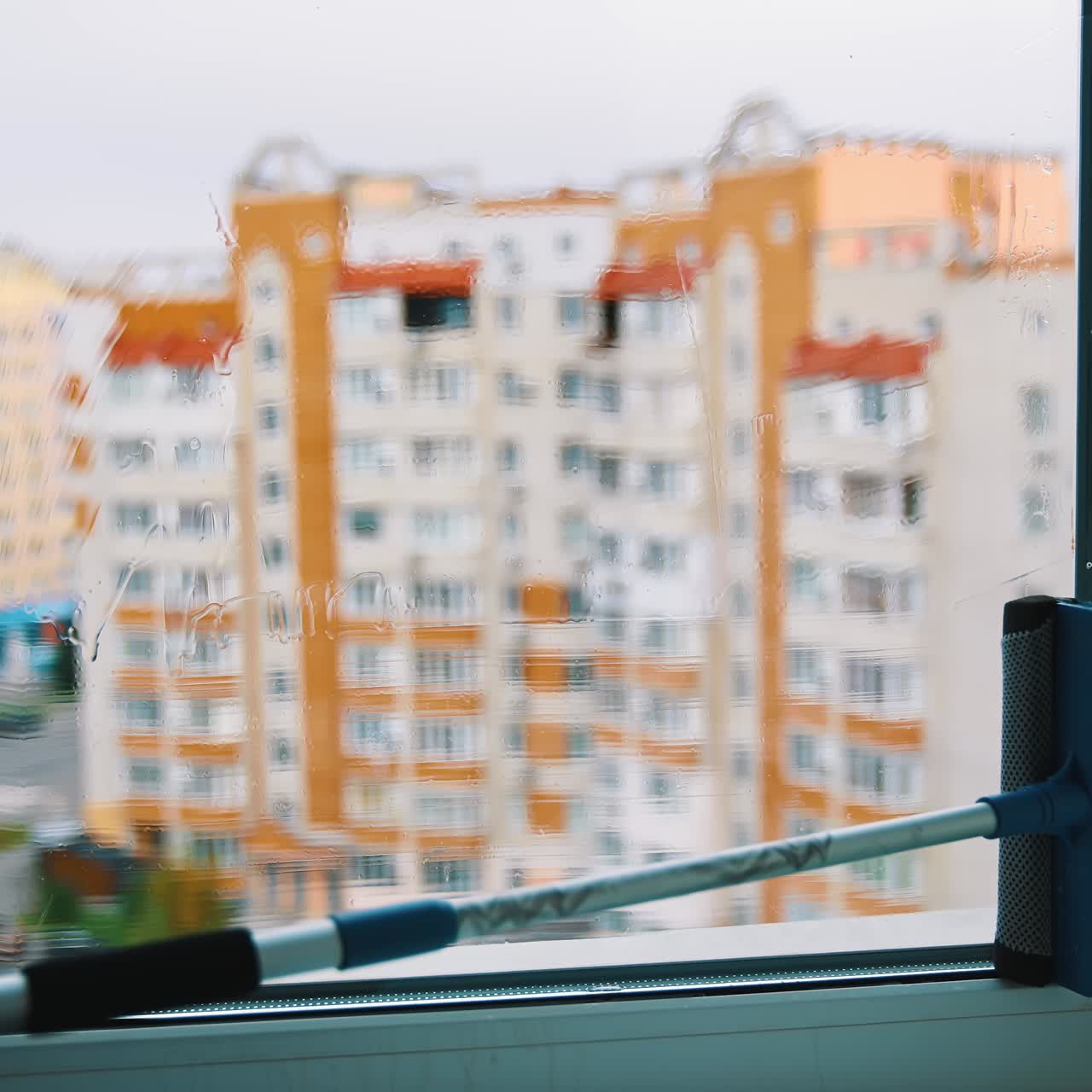 Window cleaning brush making glass clean. House worker washing window with a special brush inside the room on urban background