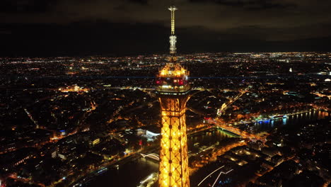 Cumbre-De-La-Torre-Eiffel-Iluminada-Con-Luz-Nocturna,-Vista-Panorámica-Del-Paisaje-Urbano-Y-Los-Horizontes-De-París,-Vista-Aérea