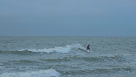 man engaged in kitesurfing, overcast winter day, high waves, baltic sea karosta beach , slow motion, distant medium shot
