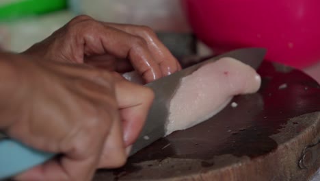 cortar carne de pecho de pollo en una tabla de madera con un cuchillo afilado