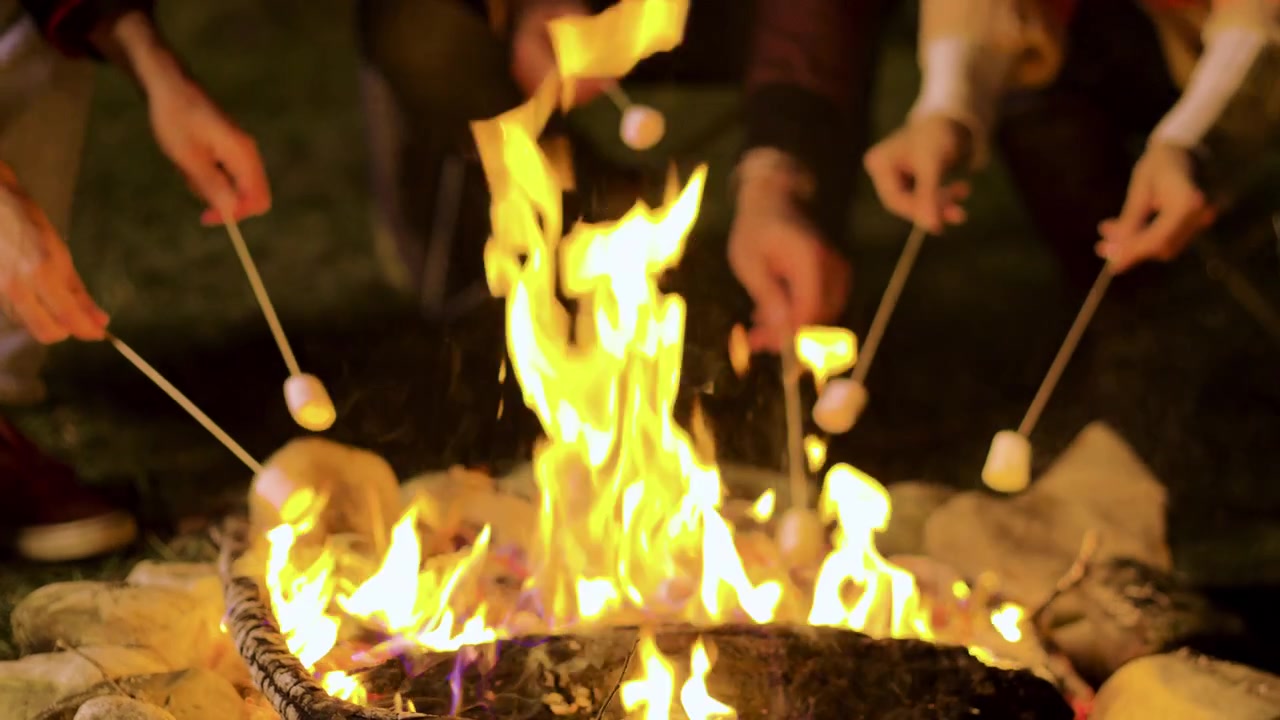 Amigos asando malvaviscos sobre una fogata de otoño