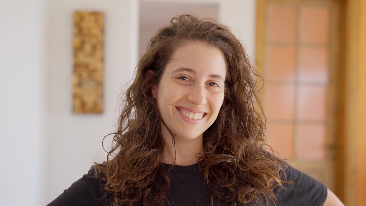 Portrait of young woman inside home or apartment smiling and cheerful looking at camera. Beautiful female with curly hair and casual clothes inside house is happy and smart looking with orange BG