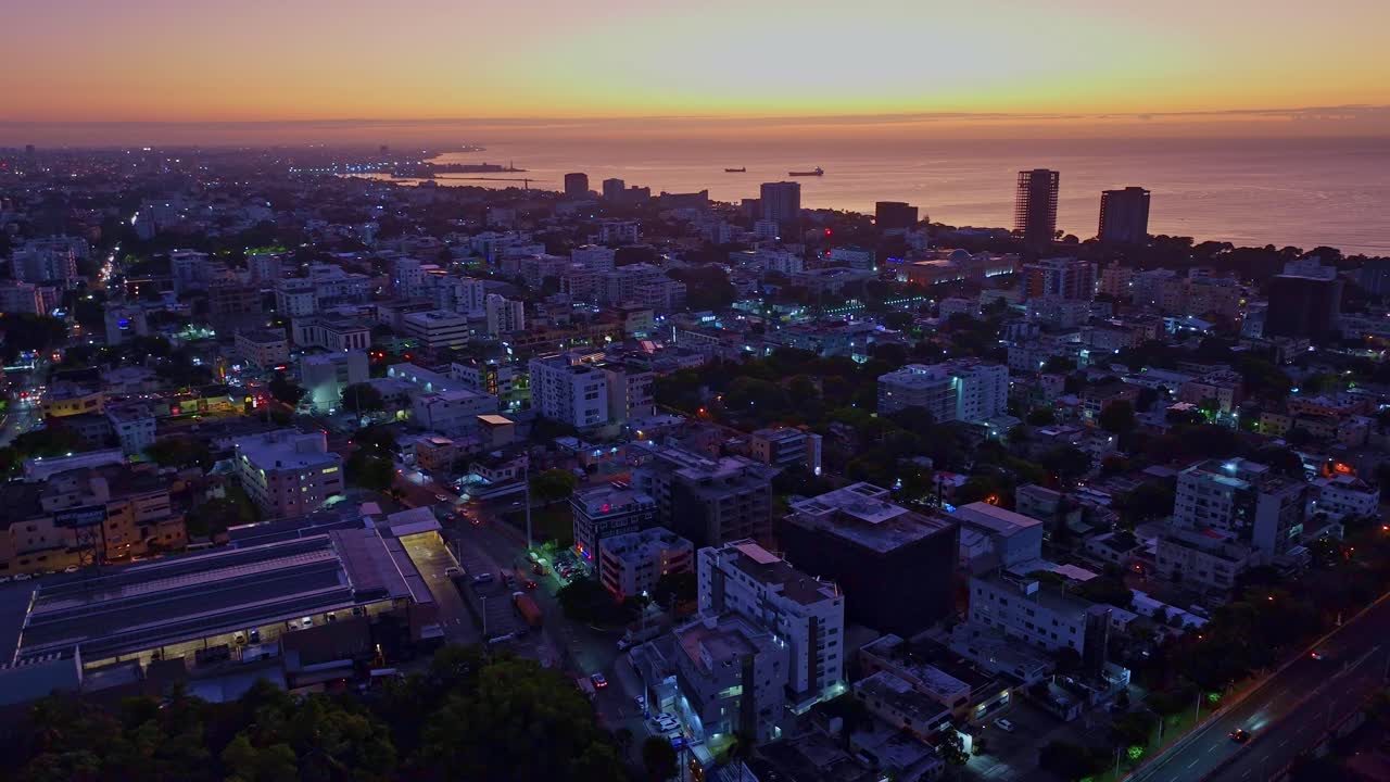 Sunrise over Santo Domingo aerial shot moving forward, revealing the skyline, Caribbean Sea, and golden sunlight illuminating buildings and the horizon in a peaceful morning glow.
