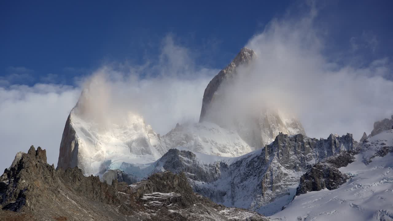 장엄한 피츠 로이 피크 (fitz roy peak) 는 은 파란 하늘 아래 회전하는 구름으로 감싸여 있습니다.