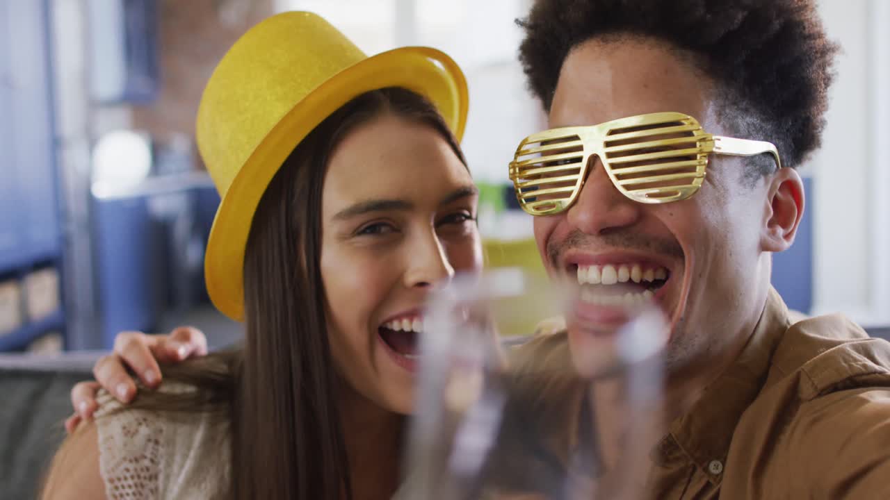 feliz pareja biracial bebiendo champán en casa haciendo una celebración llamada de video portátil y riendo