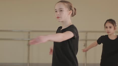 a group of young ballet students in black dancewear practicing positions in a spacious ballet studio with wooden flooring and wall-mounted barres. focused expressions and synchronized movements.