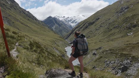 young caucasian woman walking and looking around in a valley in between mountains on a sunny summer day in rees dart track, new zealand