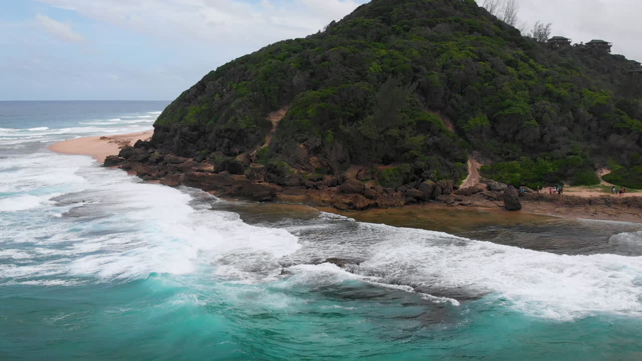 vista aérea panorámica del océano en una isla privada con olas salpicando rocas con gente caminando en la playa