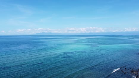 Aerial-drone-view-rising-over-coral-reef-ecosystem-and-expansive-turquoise-ocean-water-with-a-glimpse-of-mainland-Timor-Leste-in-distance