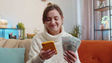 Mujer-Joven-Sonriente-Y-Feliz-Contando-Dinero-En-Efectivo,-Uso-De-Ingresos-Por-Teléfono-Inteligente,-Ahorra-Lotería-Y-Gana-El-Presupuesto-En-Casa