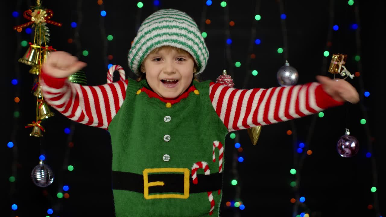 Náctiletá dívka v kostýmu vánočního elfa / pomocníka Santa Clause ukazuje palec nahoru na černém pozadí