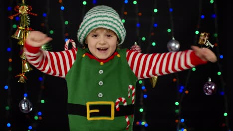 Teen-kid-girl-in-Christmas-elf-Santa-Claus-helper-costume-showing-thumbs-up-on-black-background