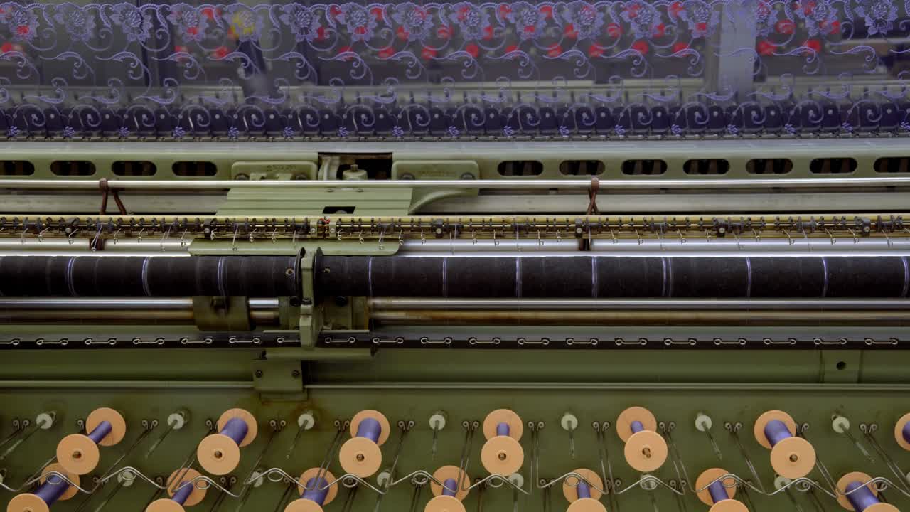 Máquinas têxteis industriais com bobinas de linha produzindo tecidos de renda.