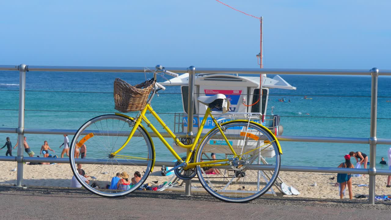 Yellow bicycle with basket parked against a barricade in bondi beach. Bicycles stand after cycling and riding. Bicycles are illuminated by the sunset sunbeams.Slow Motion Of Yellow Bicycle Parked.