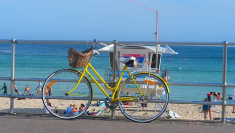 Yellow bicycle with basket parked against a barricade in bondi beach. Bicycles stand after cycling and riding. Bicycles are illuminated by the sunset sunbeams.Slow Motion Of Yellow Bicycle Parked.