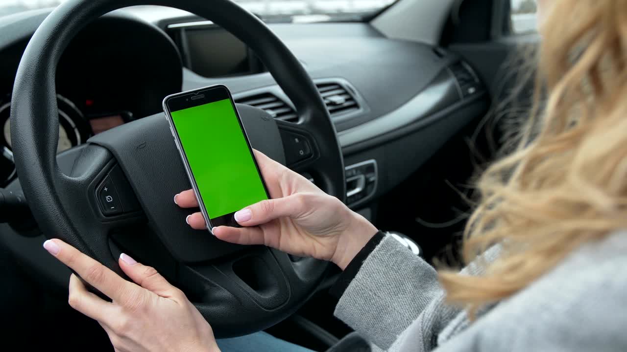 mujer se sienta en el coche moderno y usando el teléfono inteligente - manos de primer plano. pantalla verde. llave croma