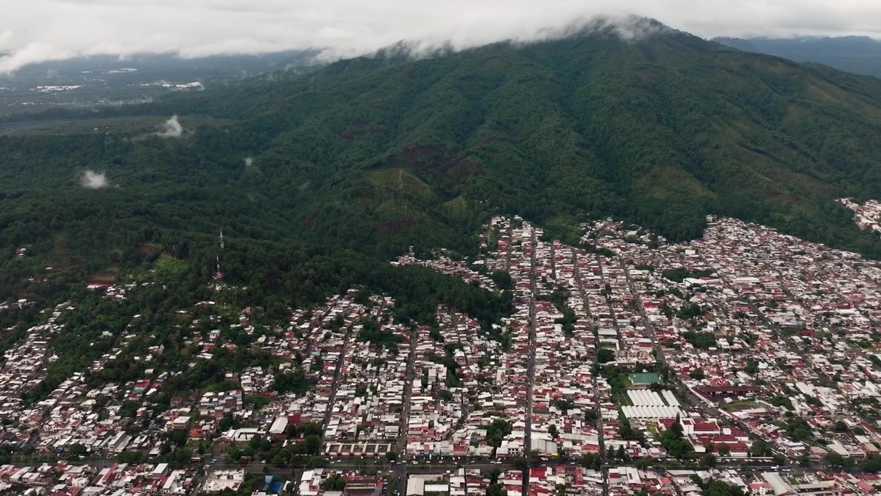 Sfondo aereo dei quartieri di Uruapan che confinano con pendii montani boscosi, drone che stabilisce lo sfondo tracciando a destra.